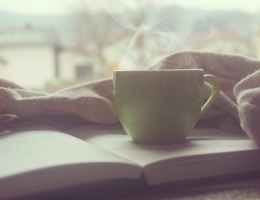 An open book with a warm drink on top.
