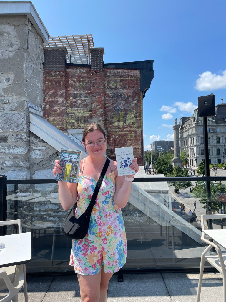 A girl standing in front of buildings, holding two books.
