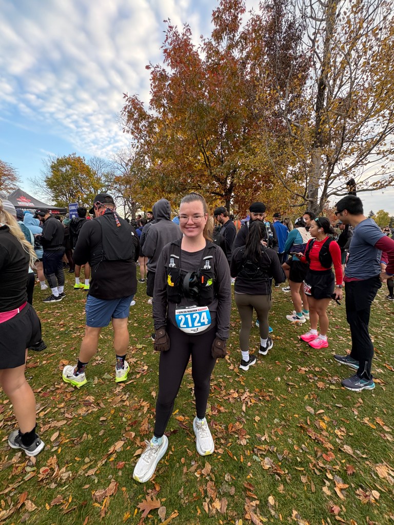 A girl standing on a patch of grass before a running race. She is wearing dark running clothes and a pair of white shoes.