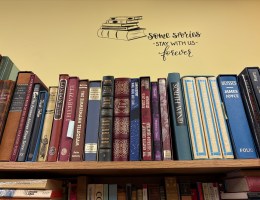 A bookshelf at a bookstore with a vinyl graphic above on the wall that reads 'some stories stay with us forever.'